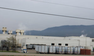 An image of the outside of a Bush Brothers factory. Shipping truck loads are in front of the factory and mountains lay in the background.